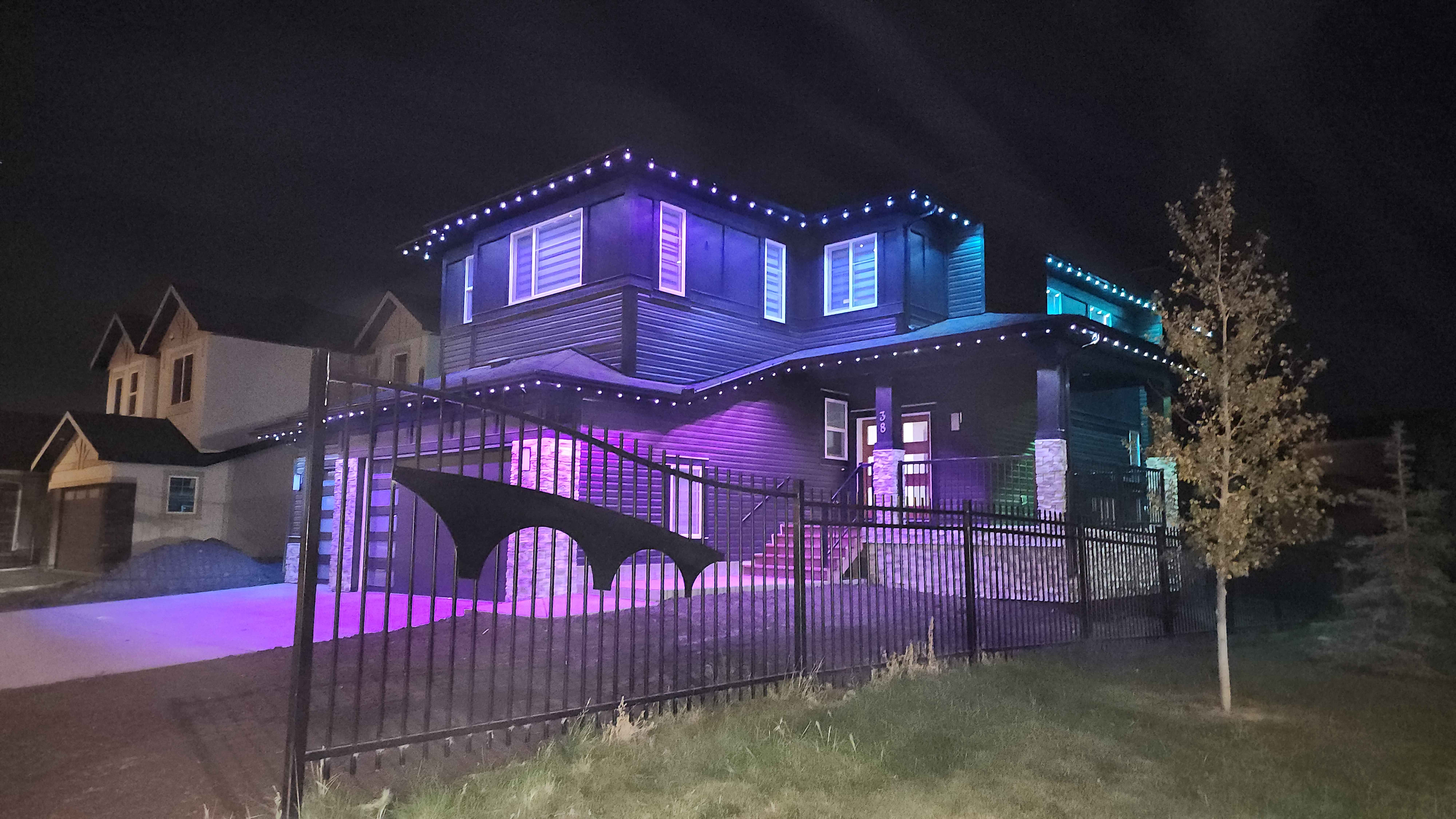 Two-storey home washed in blue and teal behind a wrought-iron fence