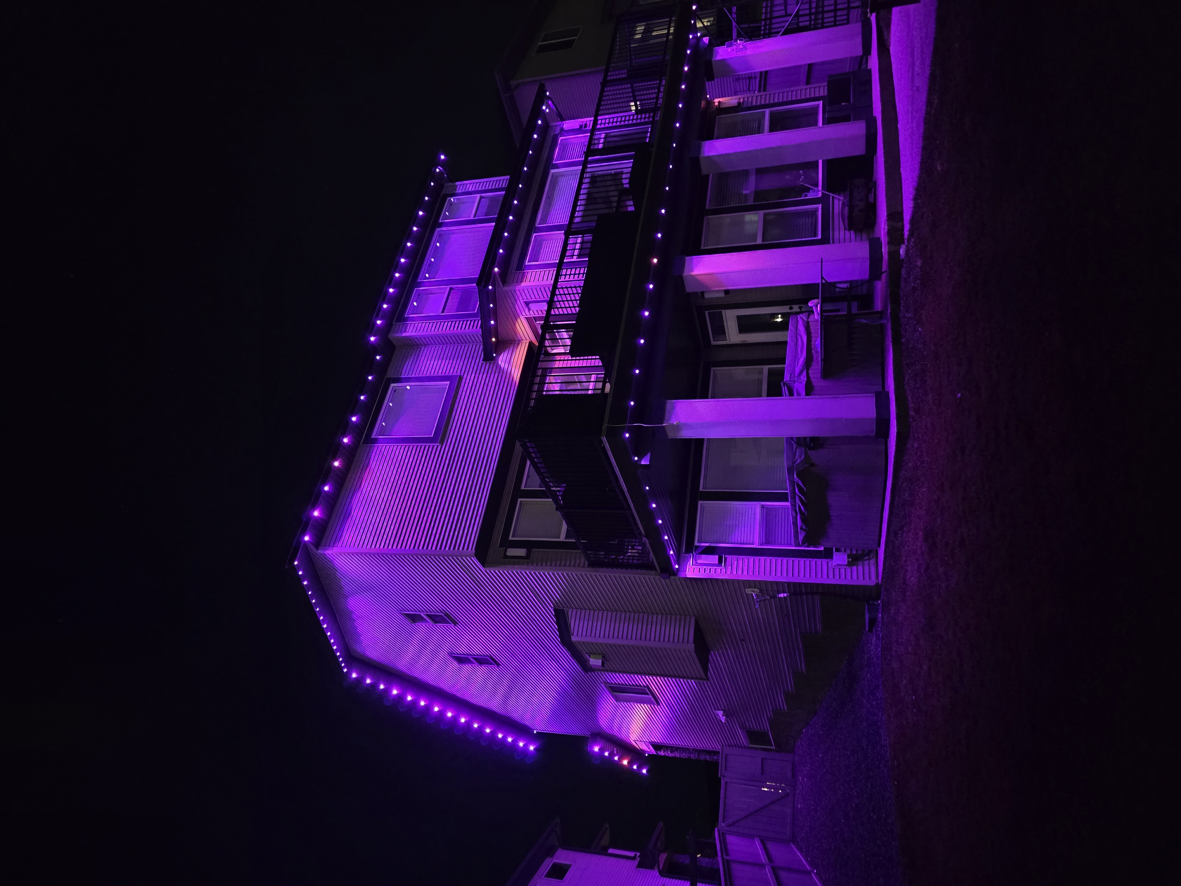 Back of a three-storey home and covered deck washed entirely in purple permanent lights